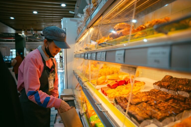 A bakery employee wears an apron and organizes pastries in a well-lit Baguio store.